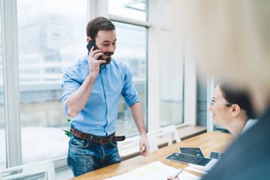 Gözlüklü, gülümseyen bir kadın masada oturmuş mavi gömlekli, sakallı bir erkeği izliyor.