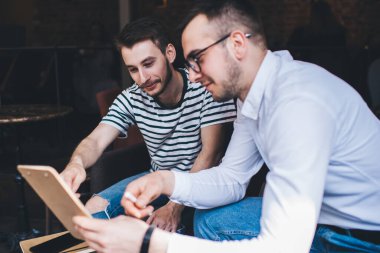 Rahat bir restoranda oturup birlikte çalışırken, günlük kıyafetli, gülümseyen ve iş arkadaşı için panoya işaret eden genç adam.