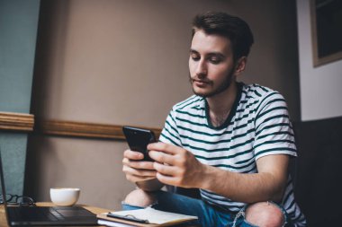 Akıllı bir adam masadaki koltukta dizüstü bilgisayarı ve koyu ışıklı bir fincan kahveyle oturup sörf yapıyor. 