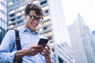 New York, Manhattan 'da gökdelenin önünde ofis kıyafetleri içinde modern akıllı telefonlara göz atan genç ve yakışıklı bir adamdan.