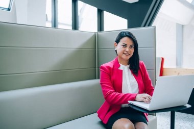 Beyaz bluzlu ve siyah etekli İspanyol kadın kanepede oturuyor ve kameraya bakıp gülümsüyor.