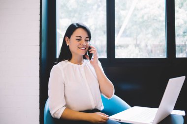 Deneyimli bayan müdür yardımcısı cep telefonuyla konuşuyor ve çağdaş ofis salonundaki netbook 'un önündeki koltukta oturuyor.