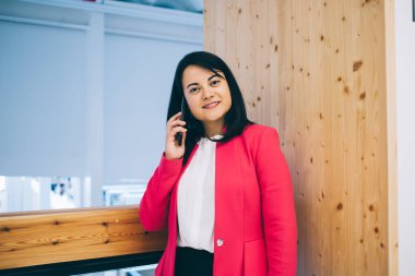 Güzel giyimli zarif ceketli bayan patron cep telefonuyla konuşuyor ve iş yerinde kameraya bakarken cevap bekliyor.