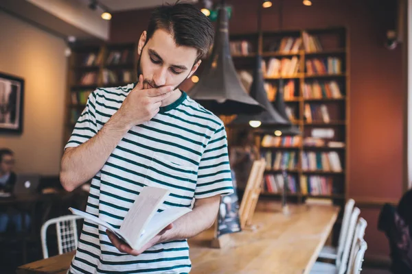 Jovem Pensativo Camiseta Listrada Esfregando Queixo Lendo Livro Interessante Enquanto — Fotografia de Stock