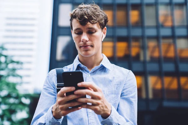 纽约高楼背景下身穿蓝色衬衫 手持手机发短信的当代帅哥 — 图库照片