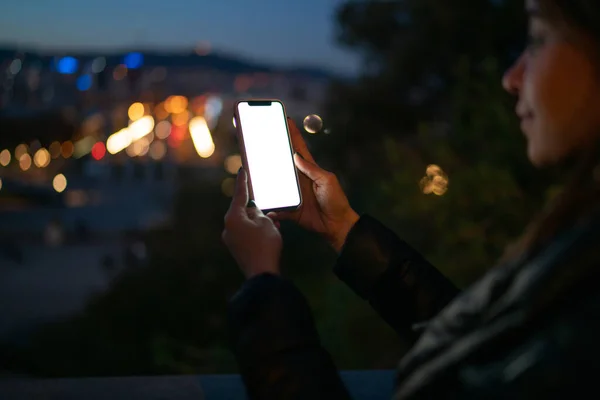 街の明かりを背景に夜に通りに立つジャケット姿の女性のミステリーサイドビューやスマートフォンの画面を見て — ストック写真