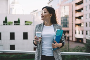 Moda ceketli ve gözlüklü çekici bir bayan öğrenci elinde kitaplarla şehir dekoruna bakıyor, gülümseyen genç hippi kız işten zevk alıyor kahve molası verip kahve içiyor. 