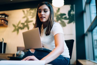 Dizüstü bilgisayar kullanan ve iş yerinde yeni bir proje üzerinde çalışırken kağıt belgelerine bakan genç ve yaratıcı kadın serbest yazardan.