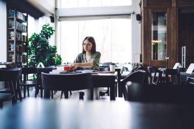 Zeki, ciddi bir kız öğrenci siyah masada boş ışık kütüphanesinde ders çalışmak için bir sürü yeri olan kitaplarla oturuyor.