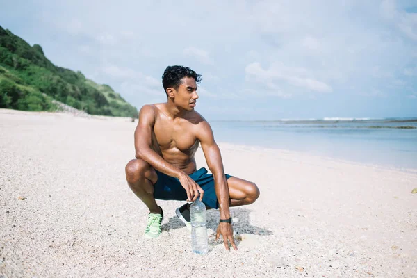 砂の上にスクワットや水のボトルを保持しながら海を見て — ストック写真