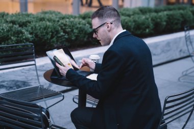 Girişimcinin resmi kıyafetlerini akıllı telefon kullanarak ve kahve masasında otururken tablet üzerinde klavyeyle çalışırken yandan görünüşü