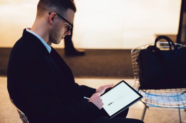 Resmi gözlüklü ciddi tasarımcının yan görünüşü sandalyede oturuyor ve Stylus ile modern tablete çizim yapıyor.
