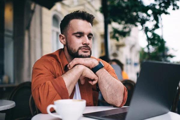 Příjemný Pohledný Muž Sleduje Internetové Články Notebooku Opřenou Bradou Ruce — Stock fotografie