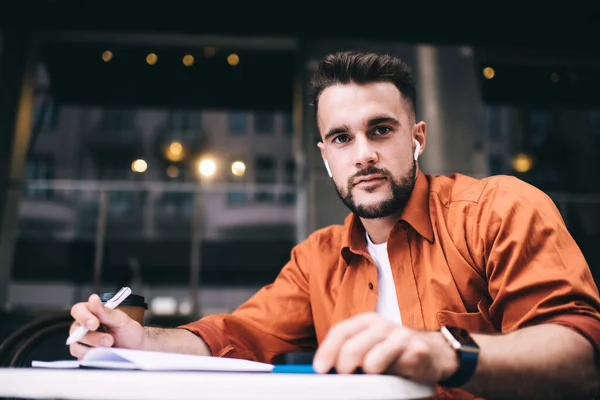 Bello Uomo Hipster Barbuto Auricolari Camicia Arancione Seduto Nel Caffè — Foto Stock