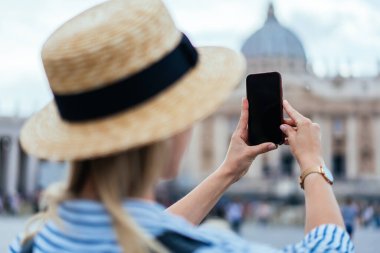 Hipster bayan gezginin Vatikan 'da heyecan verici bir turda meydanda dikilirken akıllı telefonuyla fotoğraf çekmesini yan görüyorum.