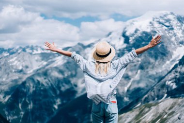 Yazlık şapkalı şık bir kadının, kollarını uzatıp, güneşli bir günde Lago di Braies yakınlarında dağ sırtına karşı özgürlüğün tadını çıkarışının arkası.