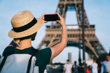 Fransa gezisi sırasında Paris caddesinde dikilirken Eyfel Kulesi 'nin fotoğraflarını çeken yaz şapkalı bayanın arka görüntüsü