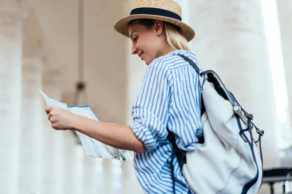 Beautiful Caucasian backpacker reading paper map during vacation holidays for visiting popular historic places, charming woman holding navigation guide for search route way and walk during journey