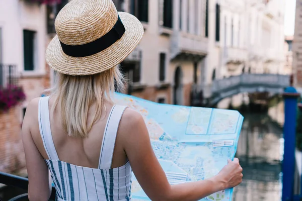 意大利威尼斯度假时带着浅色头发头戴帽子的女人站在地图上的背影 — 图库照片