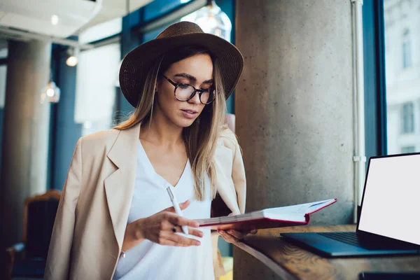 Pretty Young Freelancer Stylish Glasses Hat Checking Notes Notebook While — Stock Photo, Image