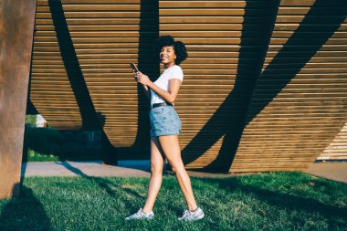 Beyaz gömlekli, şortlu, kıvırcık saçlı ve yazın sokakta gezen mutlu bir etnik bayan. 