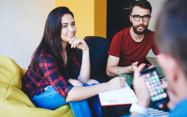 Tarayıcı web sitesi ile cep telefonu tutan adamın kırpılmış görüntüsü iş arkadaşlarıyla oturan, mutlu beyaz kadın takım üyeleriyle işbirliği sürecinden zevk alan ve başlangıç fikirlerini tartışan.