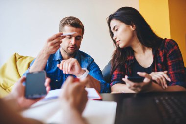 Kadın ve erkeğin yeni modern giyilebilir aletlere bakarken çekilmiş görüntüsü planlama ve organize etme için uygulamaları olan birlikte çalışma alanında oturan hippi erkekler,