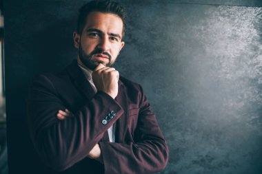 Resmi lüks ceketli yakışıklı adam duvarın yanında duruyor. Promosyon arka planında düşünceli bir şekilde kameraya bakıyor. Kapalı mekanda poz veren yakışıklı, ciddi ciddi ciddi erkek sahibinin portresi.