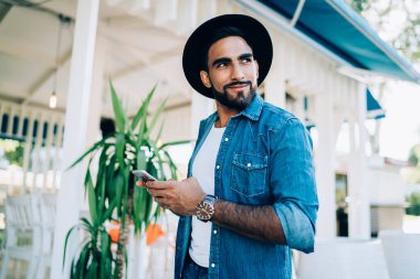 Mutlu sakallı, şık kıyafetli İspanyol bir adam. Restoranın önünde dikilip, caddede akıllı telefonlara bakarken gülümsüyor ve yüzünü çeviriyor.