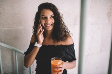 Kıvırcık saçlı, gülümseyen hippi kız cep telefonuyla sohbet ediyor. Sağlıklı yaşam tarzından tatmin olmuş taze vejetaryen kokteyliyle vakit geçiriyor.