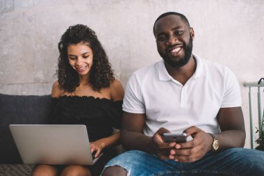 Cep telefonu teknolojisini elinde tutan neşeli erkek blog yazarının portresi kameraya bakıp gülümserken başarılı kadın serbest yazar internet sitesinde online rezervasyon yapıyor, Y jenerasyonu.