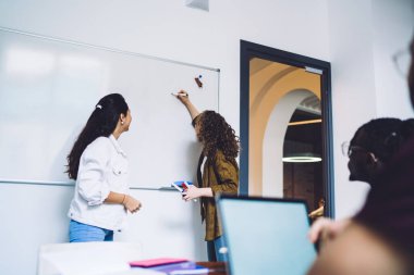 Genç başarılı çok ırklı takım iş eğitimi alıyor ve beyaz tahtaya kalemle yazı yazan kadın meslektaşları için iş fikri sunuyor.