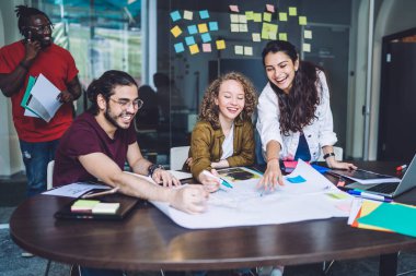 Heyecanlı kadın, elinde kalemle çizimlere işaret ederek ofiste eğlenen tasarımcılar yaratıyor.