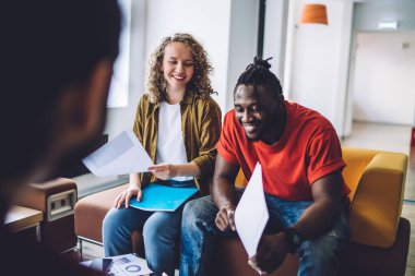 Gündelik giyim analizi yapan Afro-Amerikalı adamın, iş arkadaşları ofiste koltukta otururken ortak bir proje üzerinde çalıştığı için memnunum.
