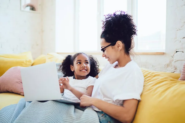 非洲裔美国母亲坐在靠近快乐孩子的黄色沙发上 用膝上型笔记本电脑看电影的侧影 — 图库照片
