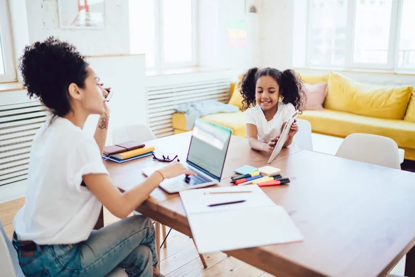 Genç etnik annenin uzaktan bilgisayarla çalışıp renkli kırtasiye malzemeleriyle modern evdeki sörf tabletinde sörf yaparken görüntüsü. 