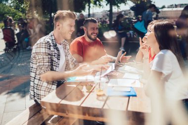 Yazın açık terasta kahve ve menü eşliğinde konuşan ve masada oturan bir grup gülen insan. 