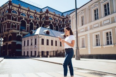 Düşük açılı, kendine güvenen, sıradan giyinen, ekranda odaklanan ve eski binaların karşısında akıllı telefonuyla iletişim kuran muhteşem bir kadın.