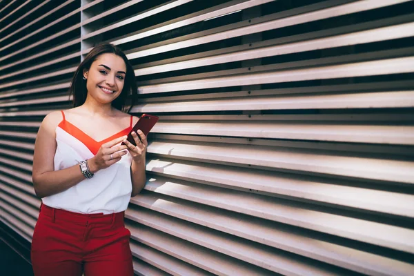 Yeni moda kırmızı ve beyaz elbiseli muhteşem bir kadın kameraya gülümserken bulanık çizgili duvara yaslanıyor ve ofisteki akıllı telefonla iletişim kuruyor.