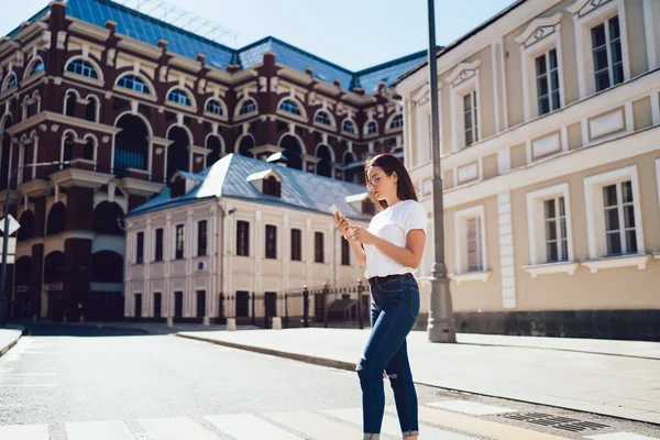 Düşük açılı, kendine güvenen, sıradan giyinen, ekranda odaklanan ve eski binaların karşısında akıllı telefonuyla iletişim kuran muhteşem bir kadın.