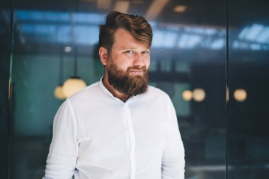 Yarım boy erkek sakallı iş adamı portresi, beyaz şık gömlekli, marka adı için fotokopi alanı olan, kendine güvenen beyaz erkek girişimci, modern çalışma alanında 30 'lu yaşlarda poz veriyor.