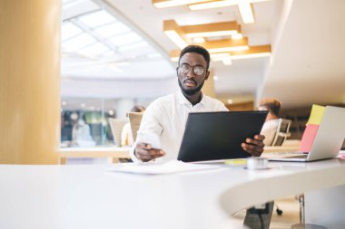 Masa başındaki muhasebe sırasında para dengesini kontrol etmek için bankacılık başvurusunda bulunan Afrikalı Amerikalı erkek girişimci, gözlüklü yetenekli işadamı akıllı telefondan posta mesajı yazıyor.