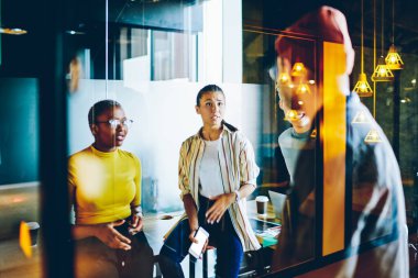 Ciddi çok ırklı kadın çalışanlar, iş planı ve problem çözme konusunda erkek liderle konuşuyor, çeşitli tasarımcılar iletişim kuruyor ve verimli işlerde işbirliği yapıyorlar.