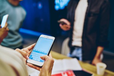Araştırma ve çevrimiçi rezervasyon için cep telefonu uygulaması kullanan, modern akıllı telefon tutan, iş yerindeki 4G aracılığıyla mesaj ve e-posta yazan bir kadının milenyum görüntüsü.