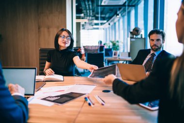 Resmi olarak giyinmiş başarılı erkek ve bayan meslektaşlar modern ofis odasında işbirliği içinde oturuyor ve belge bilgilerini, finansal beyin fırtınası kavramını analiz etmeyi tartışıyorlar.