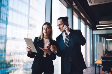 Kafkasyalı patron şirket yatırımcısıyla cep telefonuyla iletişim kurarken modern dokunmatik ekranda finansal haberler okuyor, resmi olarak giyinmiş meslektaşları ofis içi 4 G interneti olan teknolojiyi kullanıyorlar.