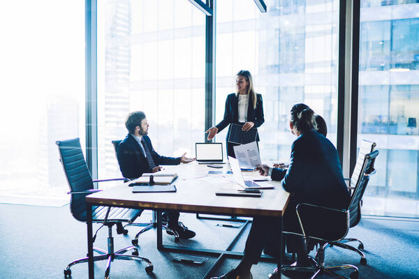 Уверенные мужчины и женщины-режиссеры, одетые для обсуждения продуктивной стратегии во время мозгового штурма на рабочем столе с ноутбуком с пустым экраном для рекламного текста или финансового сайта