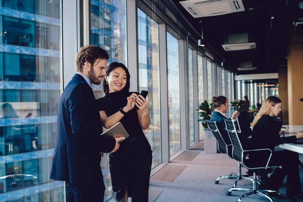 Başarılı bir kadın, erkek partnerle iletişim kurarken finansal iş videosu göstererek, modern teknoloji haberlerinde ofis kablosuyla bağlantı kuran başarılı bir şekilde giyinmiş.