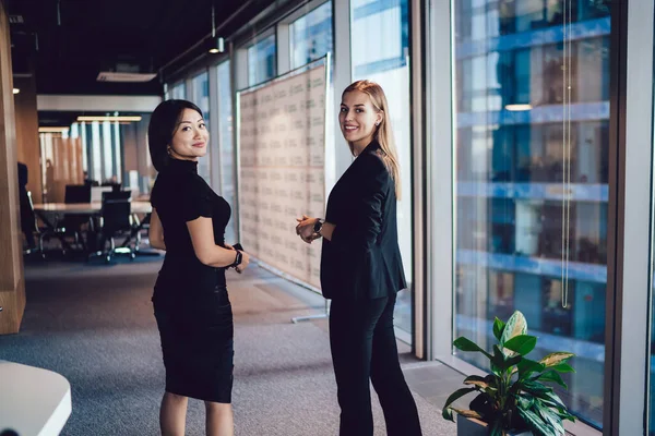 オフィスで働く若い女性従業員は 職場での友情に満たされ 企業内で一緒に歩くことで成功したキャリアを楽しんでいる女性従業員を笑顔で話します — ストック写真