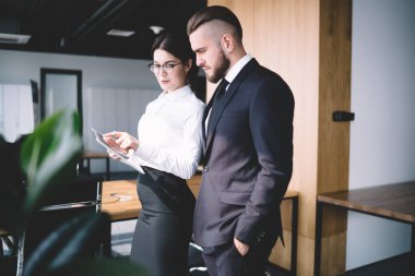 Ofiste dijital tabletle etkileşim halindeyken resmi giyinmiş ve tartışan modern erkek ve kadın meslektaşların yan görünüşü